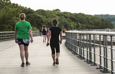 People are exercising by walking and jogging on the boardwalk at Sunken Meadow State Park next to the beach.の写真素材