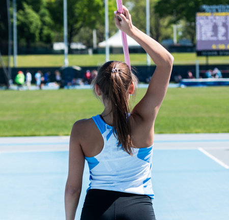 A high school girl holding a javelin overhead as she gets ready to compete in a track and field...