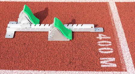 A set of track and field sprinters starting blocks are set up at the 400 meter starting line on a red track.の写真素材