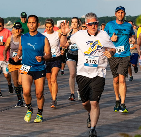 Kings Park, New York, USA - 17 June 2019: runners on the boardwalk smiling and waving at the camera...