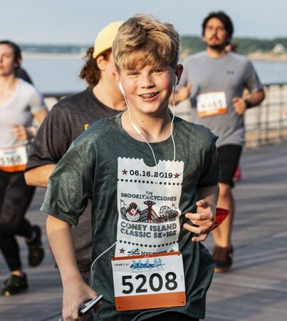 Kings Park, New York, USA - 17 June 2019: Young runner on the boardwalk smiling at the camera during the summer series 10K at Sunken Meadow State Park wearing earphones listining to music.のeditorial素材