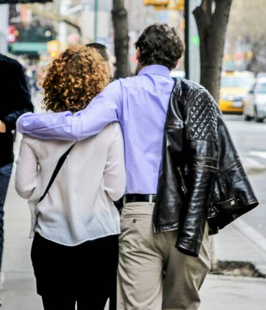 A man walking with his arm around his girlfriens shoulders and his cout over is shoulder in new york city.の写真素材