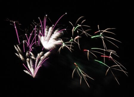 Fireworks display of pink, green and white fireworks fill the sky during a show on a summer night.の写真素材