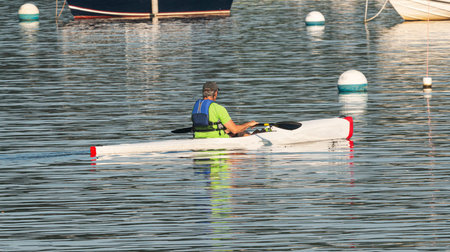 A man is enjoying a morning kayaking around moored boats on the north shore of long island in the...
