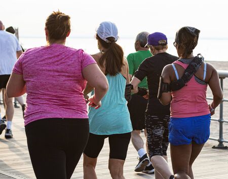 Rear View of runners racing a 10K on a boardwalk by the beach on a summer evening.の写真素材