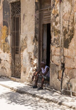 Havana, Cuba - 25 July 2018: A Cuban man is sitting on his front door step staying cool in the shade while smoking a cigarette in the city of Havana Cuba.のeditorial素材