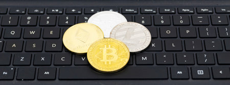 Bitcoin, litecoin, ethereal and ripple coins on top of a black computer kerboard with white letters.