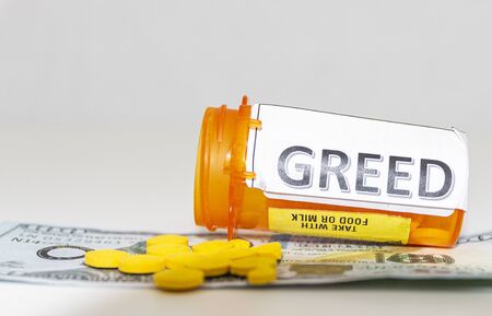 Yellow pills on a one hundred dollar bill with a prescription pill bottle with the word greed on ot.の写真素材