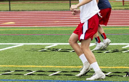 Two high school boys are running ladder drills on the turf during football summer camp.の写真素材