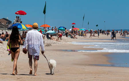 Ocean Beach, New York, USA - 27 May 2019: People enjoying a day on the beach at Ocean Beach on Fire Island, walking their dog, playing in the water and relaxing on the sand.のeditorial素材