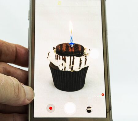 A cookies and cream cupcake with a blue candle burining on top being recorded by a cellphone.の写真素材