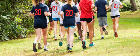 Rear view of a high school cross country team training in a group on a grass path in a local park.