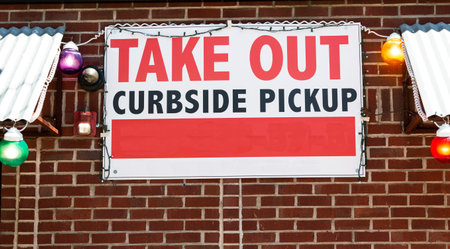 A restaraunt has a Take Out Only and Curbside pick up sign posted on the brick wall of their...