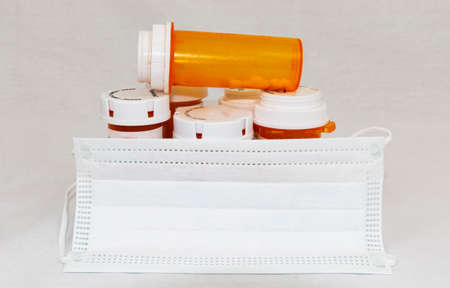 Babylon, New York, USA - 11 April 2020: A white surgical mask covering perscription medical bottles with opiods in them with a whte background.のeditorial素材