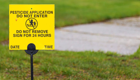 A yellow sign place on a residential lawn reads Pesticide applicatiion, do not enter for 24 hours.