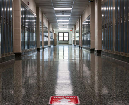 An empty high school hallway with one way sign taped on the floor as part of the neew normal for opening up schools in a pandemic.の写真素材