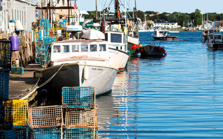 Portland, MAine, USA - 25 July 2019: Lobster fishing boats docked behind stores in a canal in Porland Maine with lobster traps and fishing tools stacked on the dock.のeditorial素材