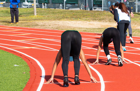 Rear view of female sprinter runners in the set position on on outdoor track during a high school...