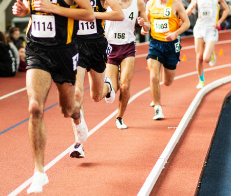 A line of runners on an indoor track racing the mile in a competative race.