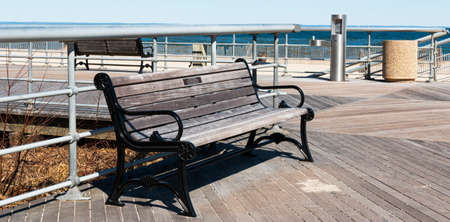 A park bench with a dedicated name plate on the boardwalk at Sunken Meadow State Park on a sunny March morning with the beach in the background.の写真素材