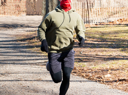 A runner is running on a trail in the woods wearing a red gaiter over his face for protection