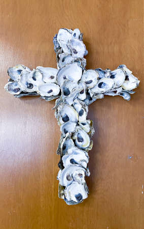 A cross made from oyster shells haning on a brown wall.の写真素材