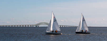 Babylon, New York, USA â 7 December 2019: Small two person sailboats in a winter regatta with the Great South Bay Bridge in the background in the waters of Long Island New York.のeditorial素材