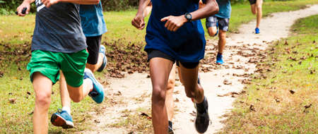 A high school boys cross country running team running fast on a dirt path covered with leaves in a local park.の写真素材