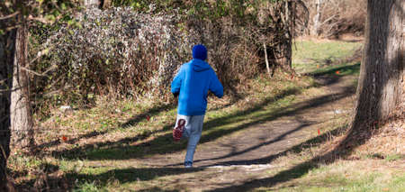 Rear view of a high school boy runing on a cross country cousrse into the woods.の写真素材