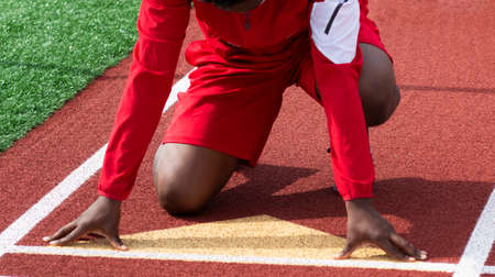 Front view of a high school track sprinter on the starting line ready to sprint down the track at practice wearing a red jacket.の写真素材