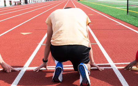 Rear view of a high school track runner is at the starting line on his mark ready to sprint down the...