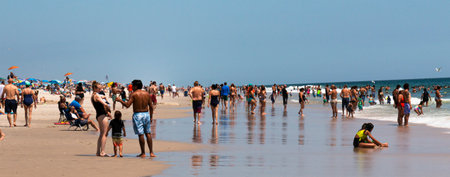 Fire Island, New York, USA - 24 July 2021: People walking, sitting and swimming by the ocean at beach where the water and the sand come together on Fire Island.のeditorial素材