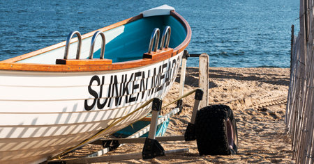 Kings Park, New York, USA - 30 Juley 2021: A white rescue lifeguards rowboat on a trailer on the sand next to a wood picket fence on the beach at Sunken Meadow State Park.のeditorial素材
