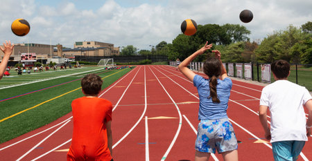 Rear view of Young teenagers throwing and chasing medicine balls down the track for strength...
