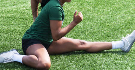 Close up of female athlete stretching in a hurdlers stretch on a green turf field.の写真素材