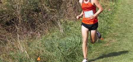 A high school boy is running on a grass field in Bowdoin Park during a cross country 5K running...