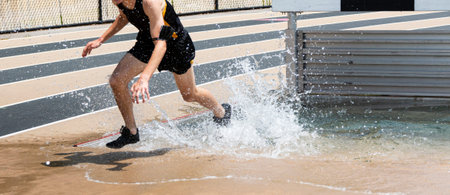 A high school boy is splashing in the water as he is exiting the steeplechase water pit during a...
