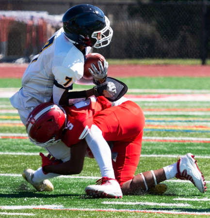 A high school football player tackling the opposing player on a turf field close up.の写真素材
