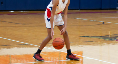 Front view of a high school basketball player dribbling the ball at the top of the key during a game.の写真素材