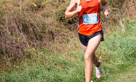 Front view of a high school boy is running in a cross country race on a grass field and a slight downhill.の写真素材