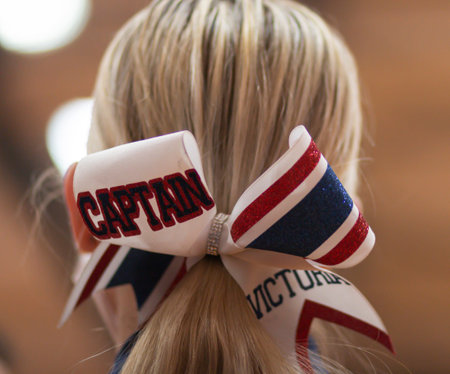 Big red white and blue bow on the back of a blond cheerleaders head with captian written on it close up.の写真素材