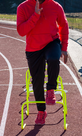 Front view of a high school runner in A-position standing over yellow mini hurdles on a track