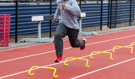 A nigh school track runner is running over small yellow mini hurdles perfomring the wicket sports...