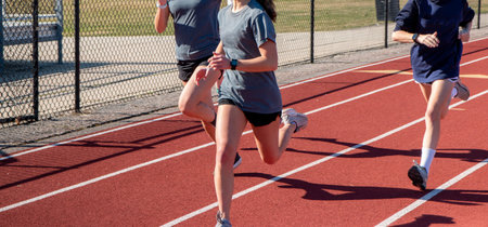 Three high school girls running fast on a red track during practice.