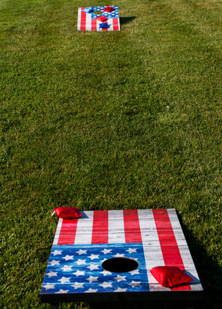 Cornhole boards painted as American flags on a thick green lawn ready for independence day parties.