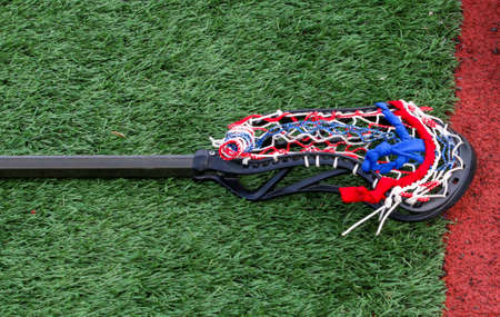 Horizontal view of a red white and blue netting on a lacrosse stick on a green turf field.の写真素材