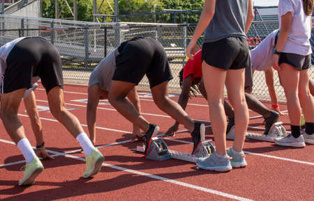 Four high school boys are set and in starting blocks ready to sprint during track and field practice outdoors.の写真素材