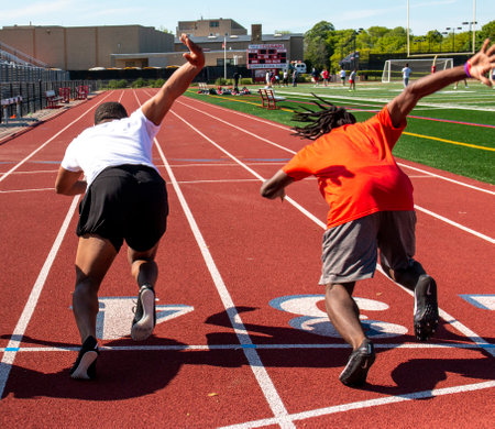 Rear view of two high school boys racing a 100 meter dash at track practice.の写真素材