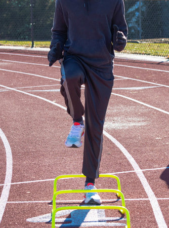 Front view ofr a runner in the A-Position standing over yellow mini banana hurdles on a track.の写真素材