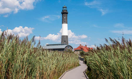 Fire Island Lighthouse and musiem building looking east with boardwalk and beach grass with a blue sky and pufffy white cloudsの写真素材